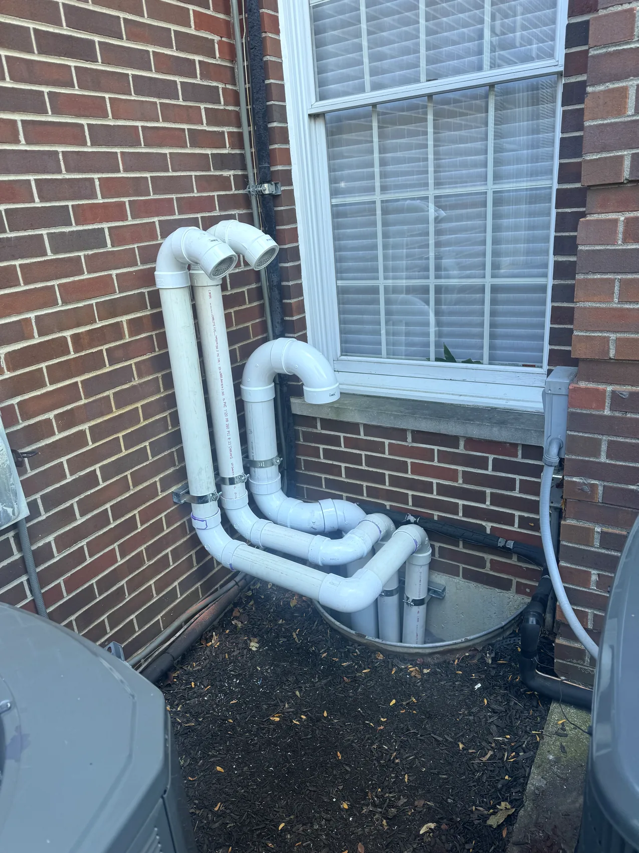 Exterior PVC HVAC drain and vent piping installed beside a brick home